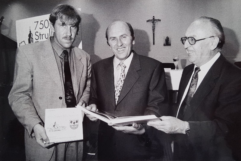 Eingerahmt vom Bürgermeister Andreas Schwarz (links) und Pfarrer Josef Ismaier (rechts) präsentiert Josef Koch das von ihm verfasste Jubiläumsbuch